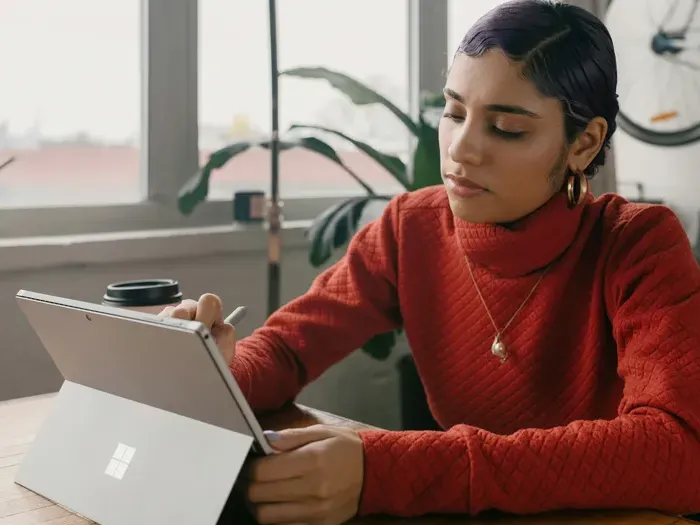 tablet device Focused woman in red sweater writing on a tablet while sitting near a window with daylight inside a modern office on Town Service Zone